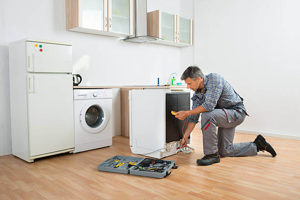 Male technician checking dishwasher with digital multimeter in kitchen